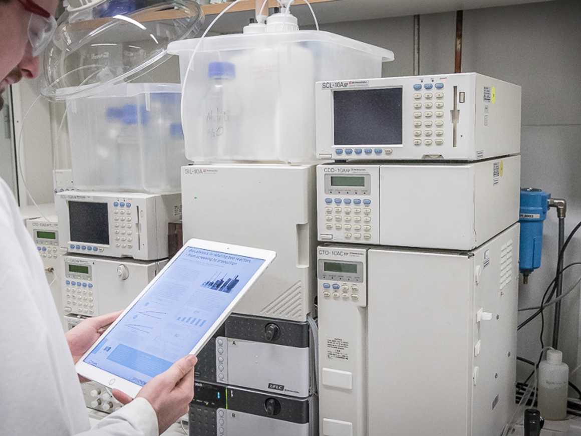 Scientist reviewing tablet data beside laboratory chromatography equipment used for chemical analysis and purification.