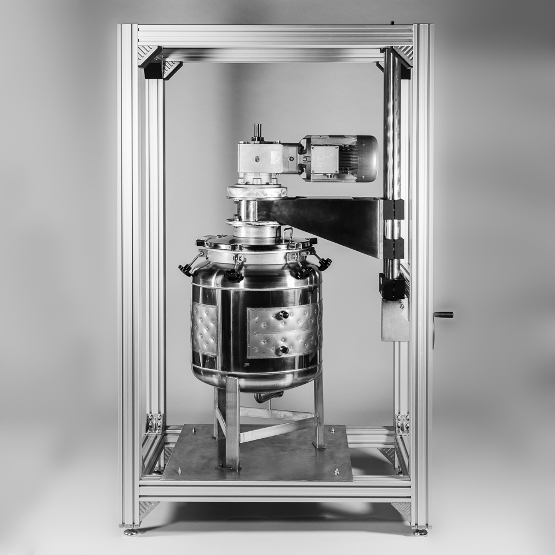 Large stainless steel reactor vessel mounted inside a rectangular metal frame with overhead motor assembly and support structure.