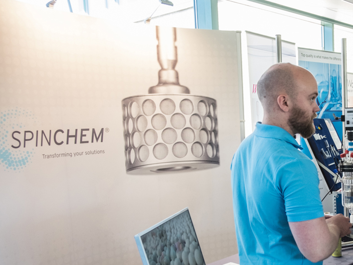 SpinChem team member presenting innovative biocatalysis solutions at a conference with rotating bed reactor displayed at the banner