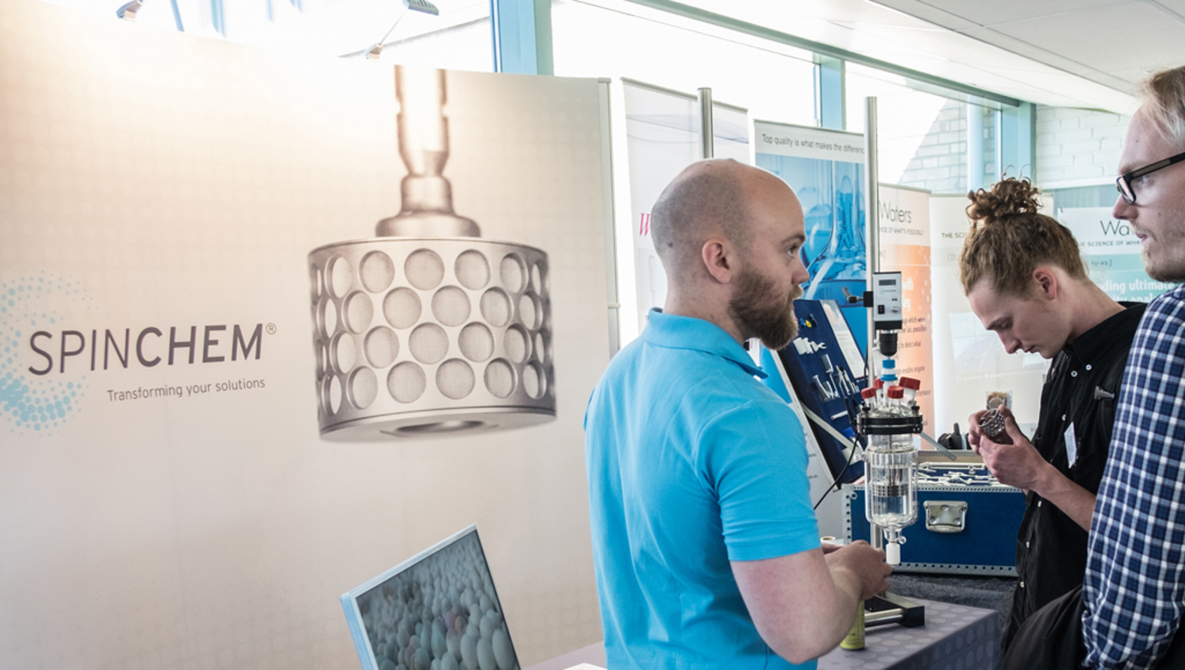 SpinChem team member presenting innovative biocatalysis solutions at a conference with rotating bed reactor displayed at the banner