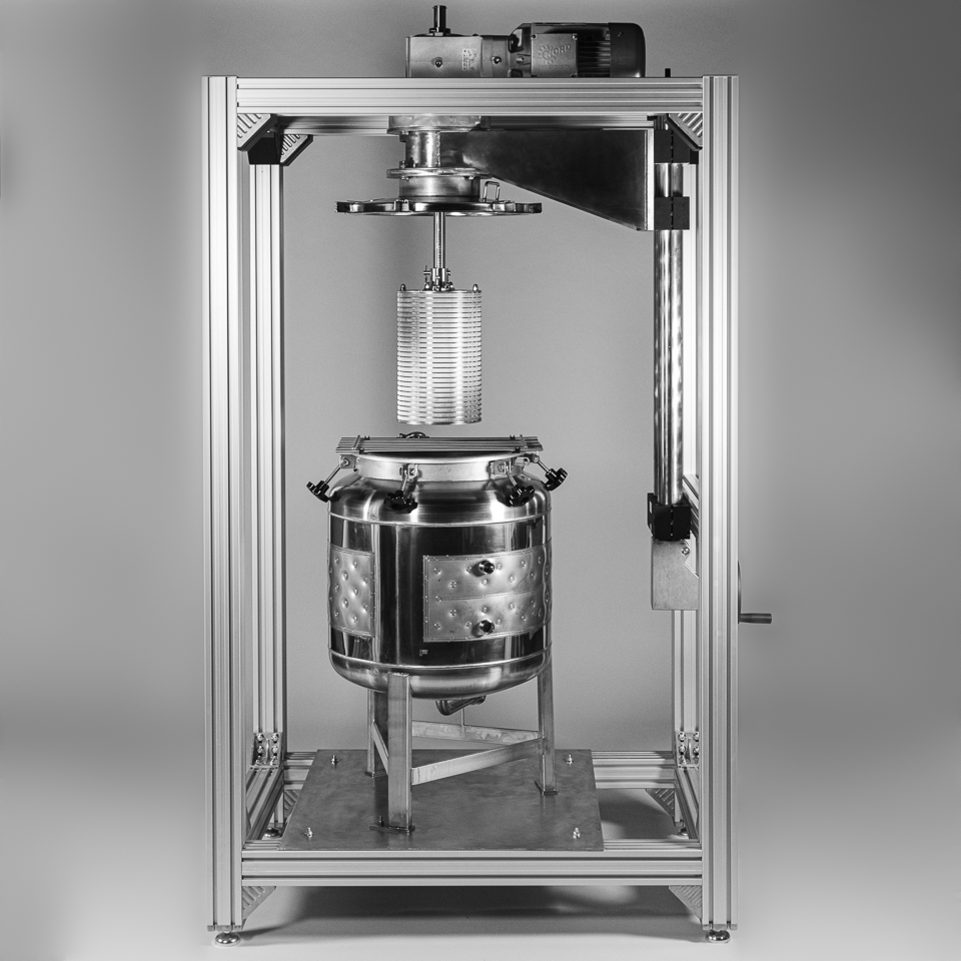Large stainless steel reactor vessel mounted inside a rectangular metal frame with overhead motor assembly and support structure.