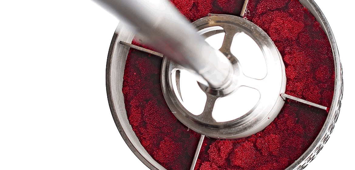 Close-up view of a SpinChem rotating bed reactor containing red ion exchange resin beads, with a metallic impeller visible in the cente